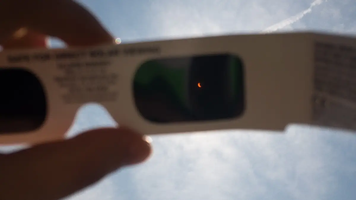 A hand holding a pair of eclipsegear 2023 solar eclipse glasses up to the sun